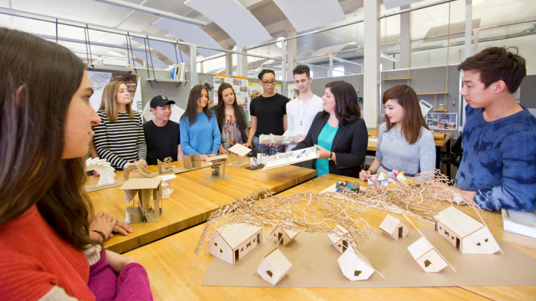 Interior design professor and students gather around models
