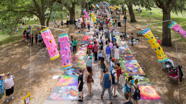 在SCAD的人行道艺术节期间，人们挤满了公园的人行道，粉红色的风结构在微风中飘扬