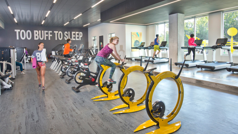 学生在现代健身房里骑着色彩鲜艳的固定黄色自行车锻炼